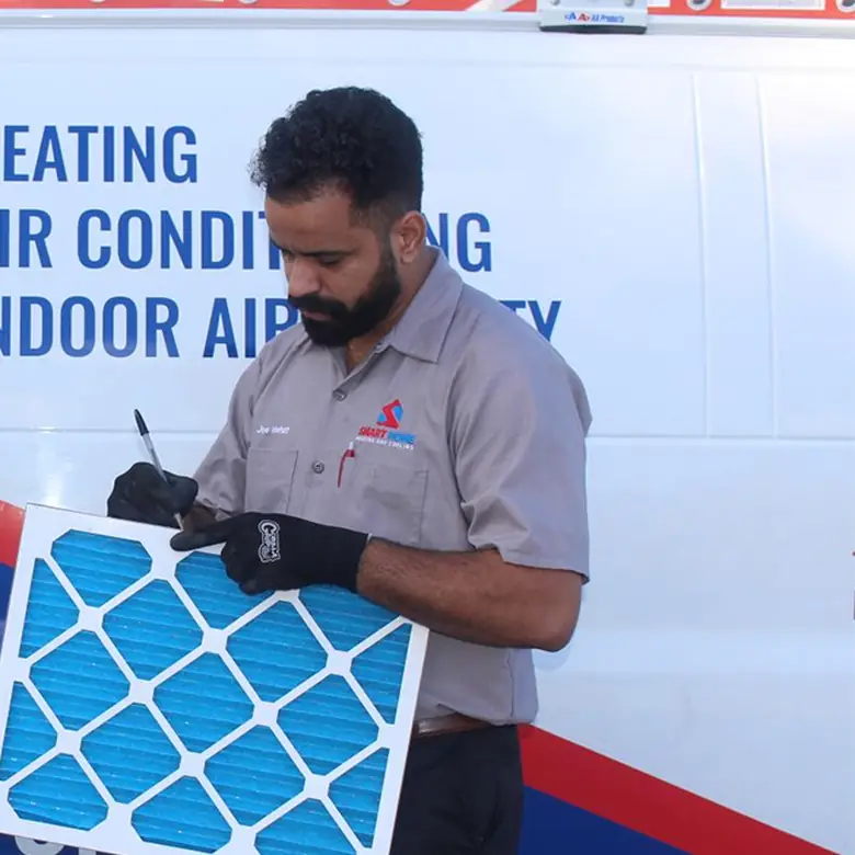 Technician writing the date on a new furnace filter beside the van